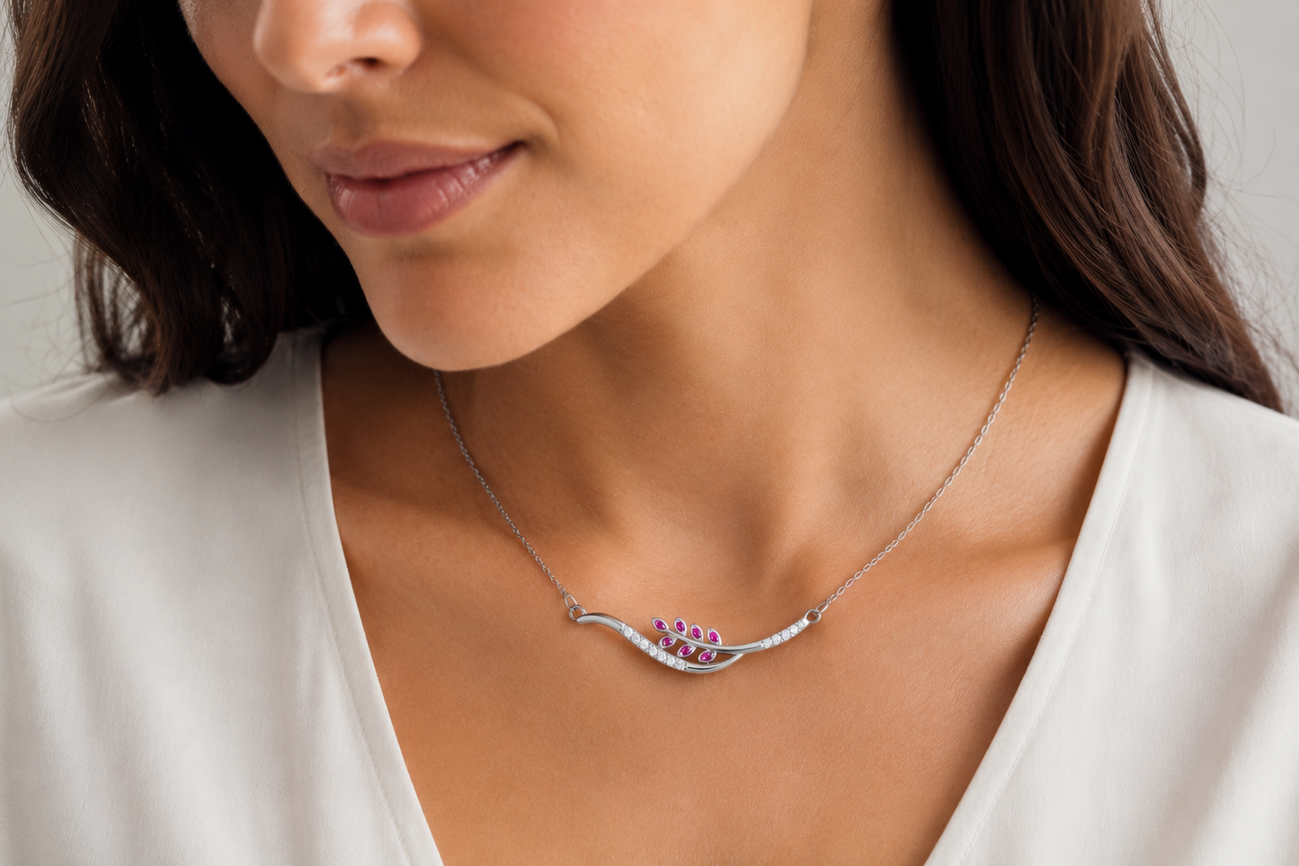 A close-up of a woman wearing a delicate JOET silver necklace with a small purple floral pendant on a white top.